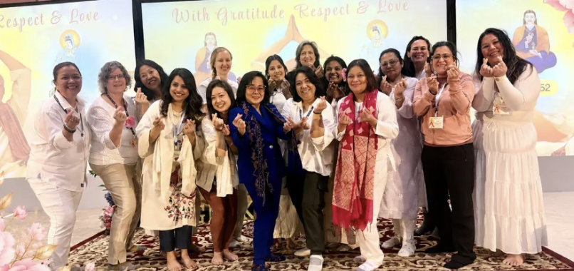 Women from the program on stage together making heart signs